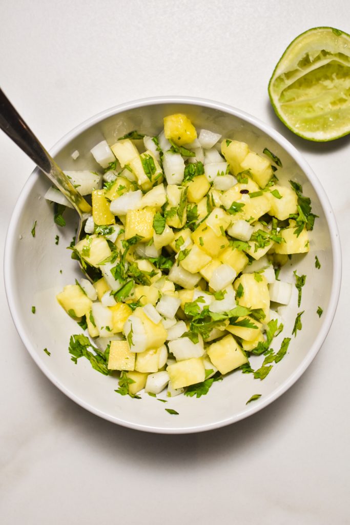 Pineapple pico de gallo mixed up in a bowl with a spoon.
