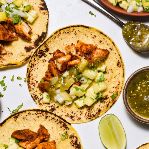 Three corn tortillas with chicken al pastor, salsa verde, and pineapple pico de gallo.