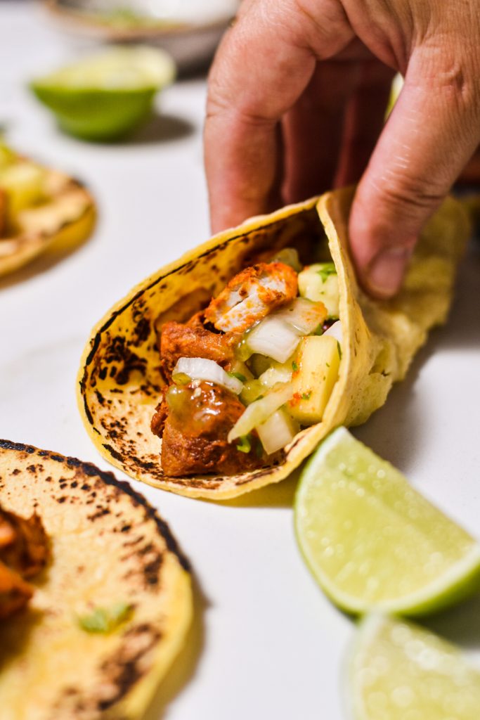 Hand holding a chicken al pastor taco together.