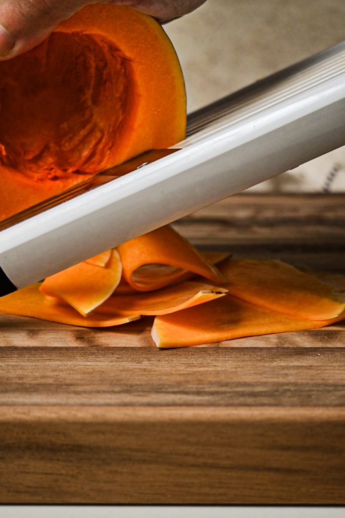 Using a mandoline to slice a butternut squash into thin slices.