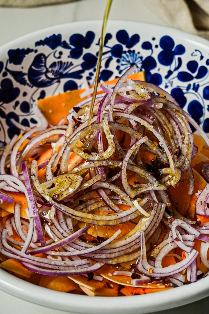 Drizzling olive oil into the butternut squash and onion mixture in a bowl