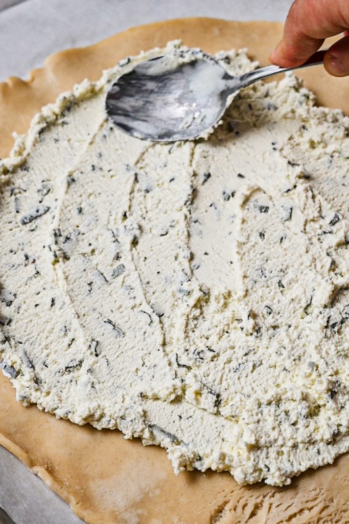 Spreading the goat cheese mixture on the pie crust with a spoon.