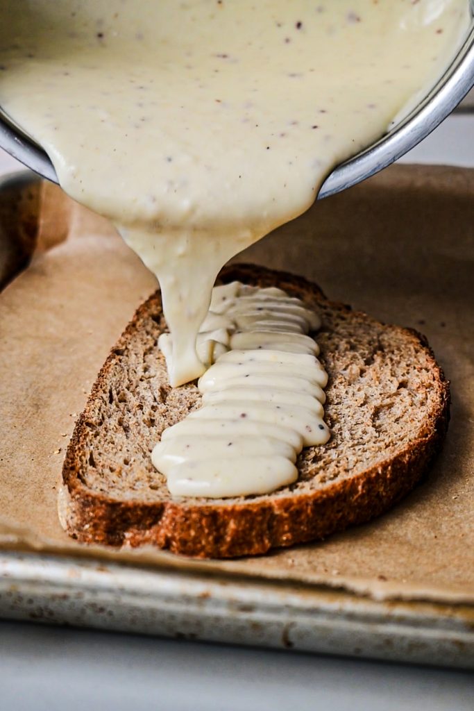 Pouring the béchamel sauce onto a piece of bread.