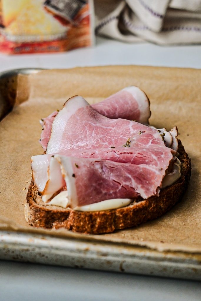 Sliced ham on top of bechamel sauce on a piece of bread.