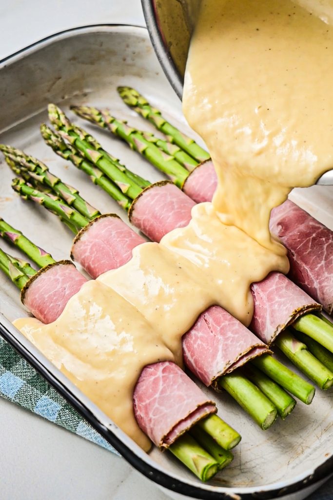Pouring the mornay sauce over the ham-wrapped asparagus bundles.