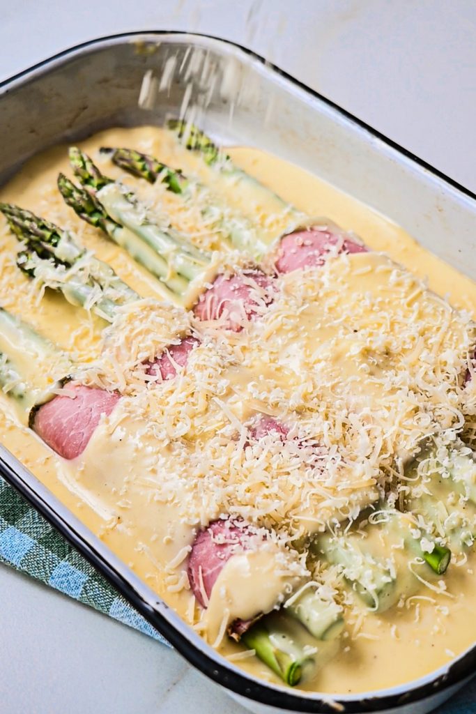 Sprinkling parmesan on top of the ham and asparagus gratin.