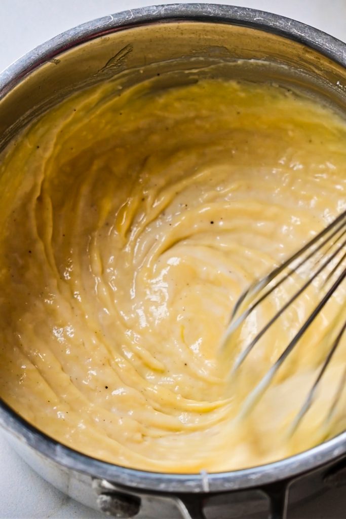 Whisking the parmesan mornay sauce in a saucepan until thick.