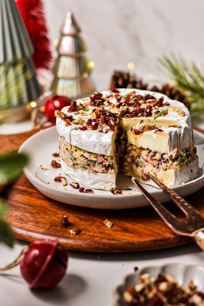 Side view of cranberry pecan stuffed brie on a plate with a slice coming out.