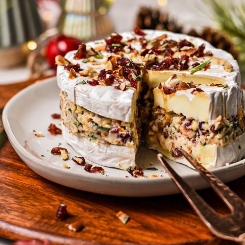 Cranberry pecan stuffed brie on a plate with a slice cut out to show the layers.