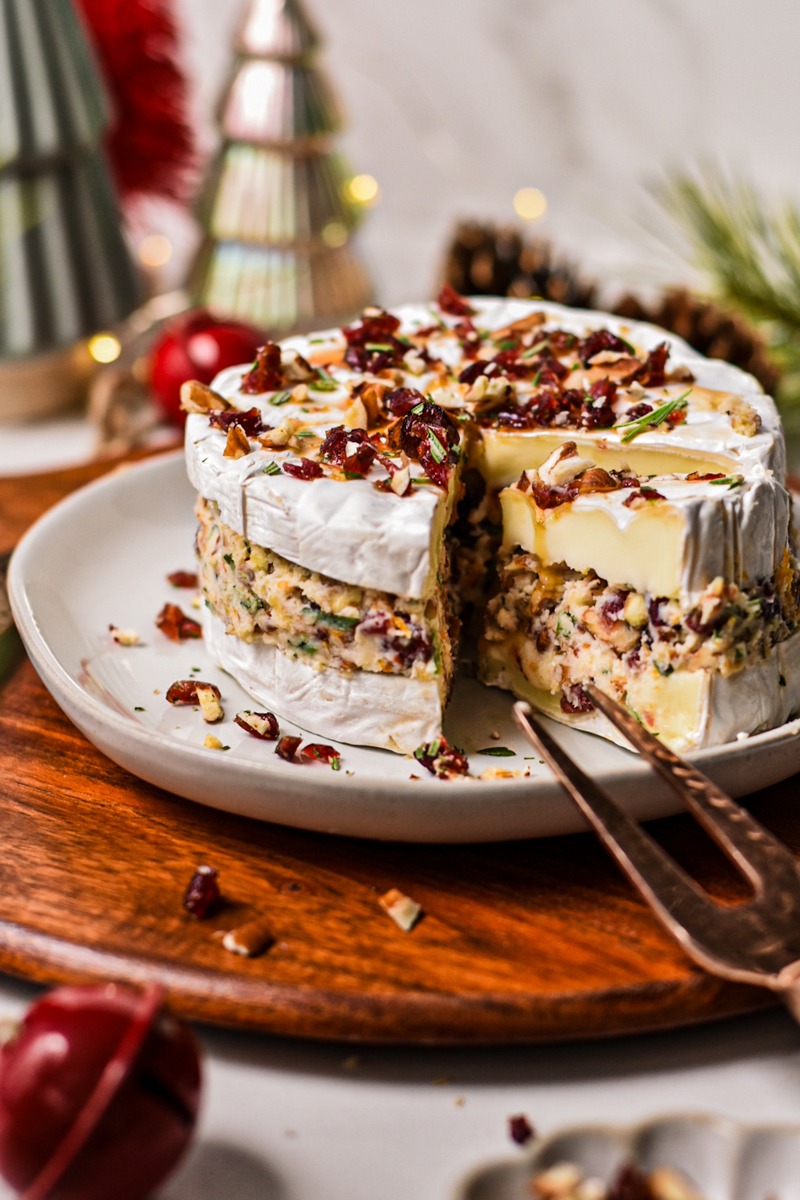 Cranberry pecan stuffed brie on a plate with a slice cut out to show the layers.