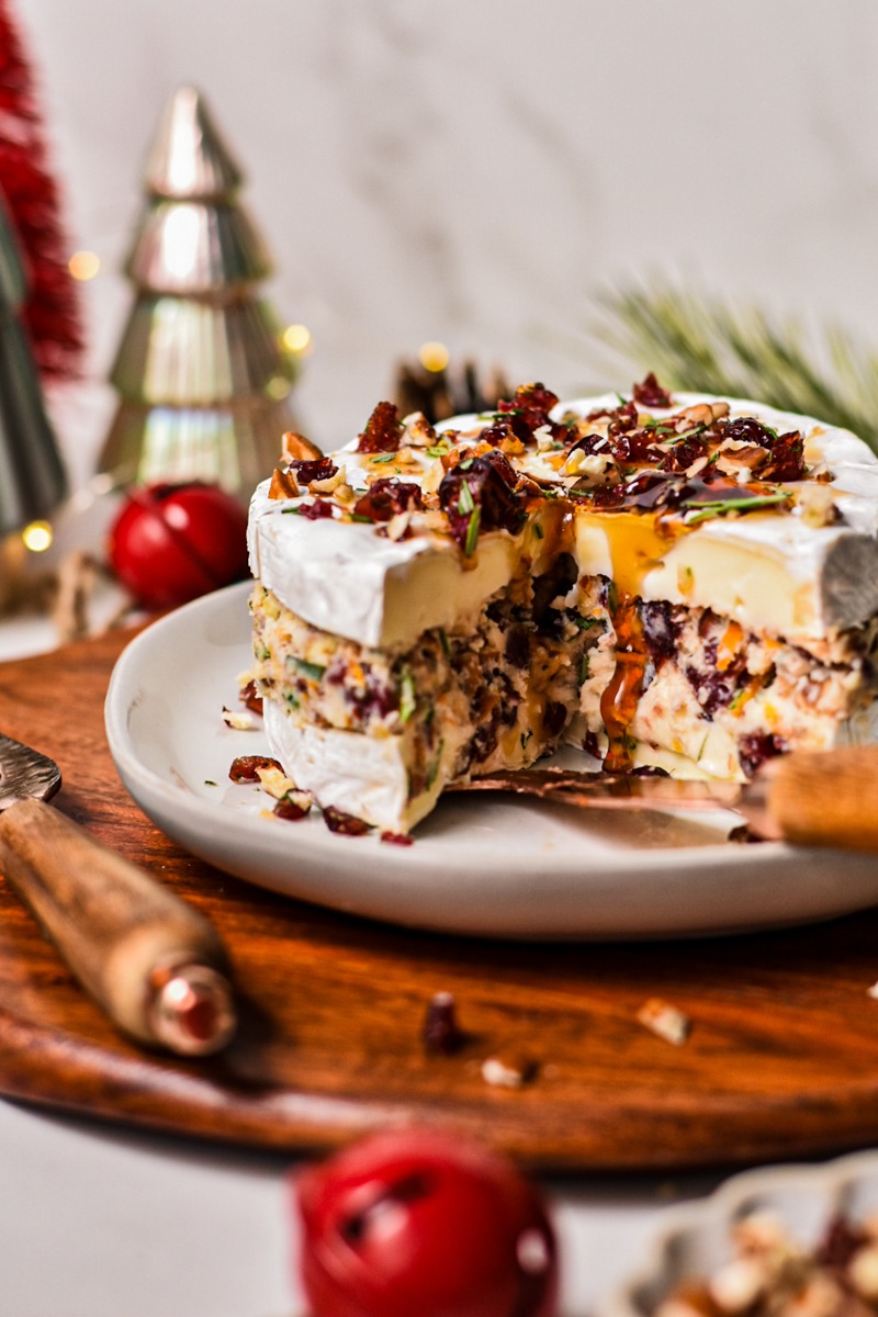 Side view of cranberry stuffed brie appetizer served on a plate on a wooden board.
