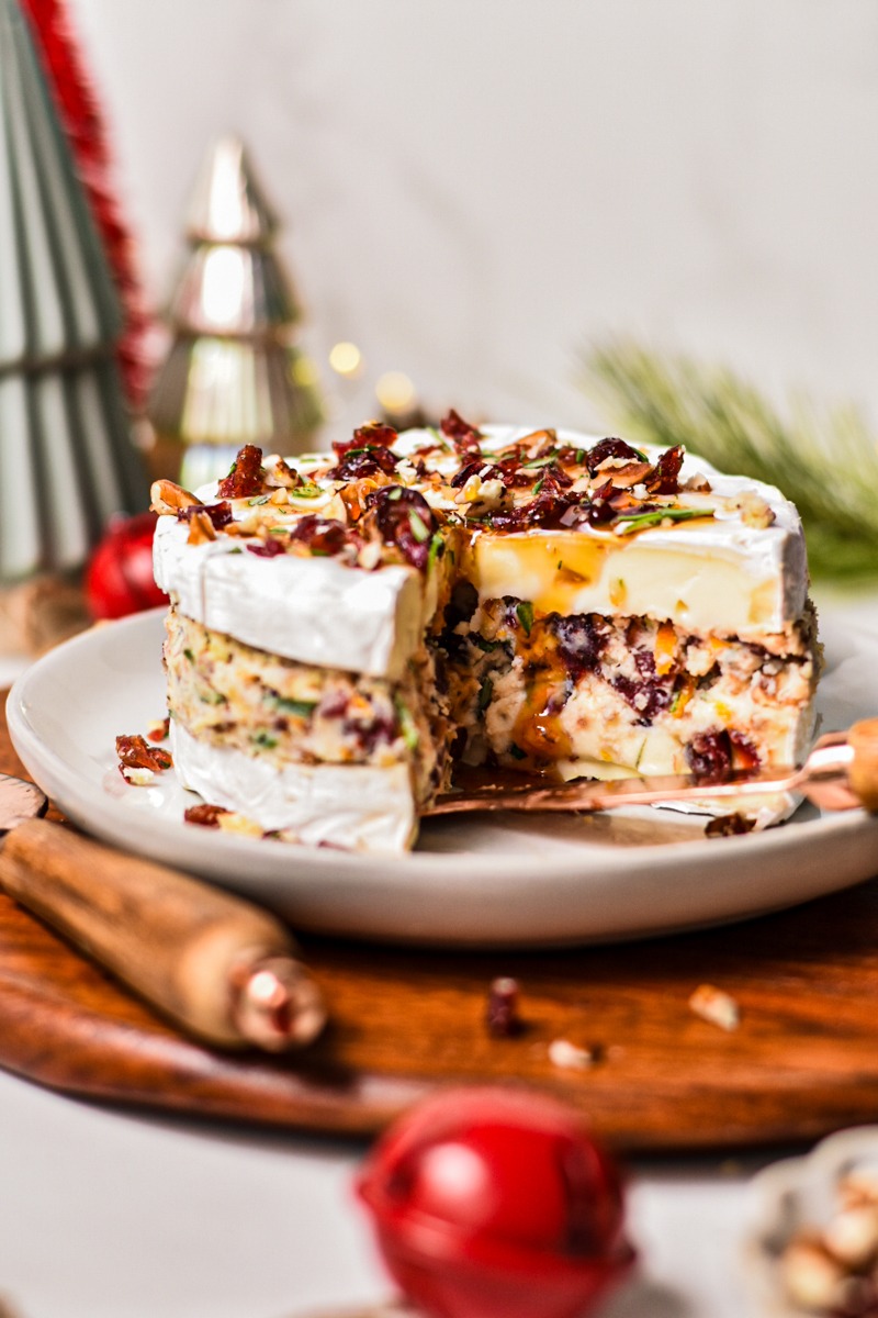 Cranberry pecan stuffed brie on a plate with a slice missing to show the inside layers.