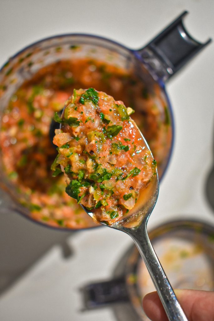 Spoon full of peach and tomato salsa hovering over the food processor of salsa.