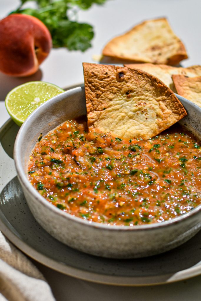 Tortilla chip in a small bowl of grilled peach and tomato salsa.