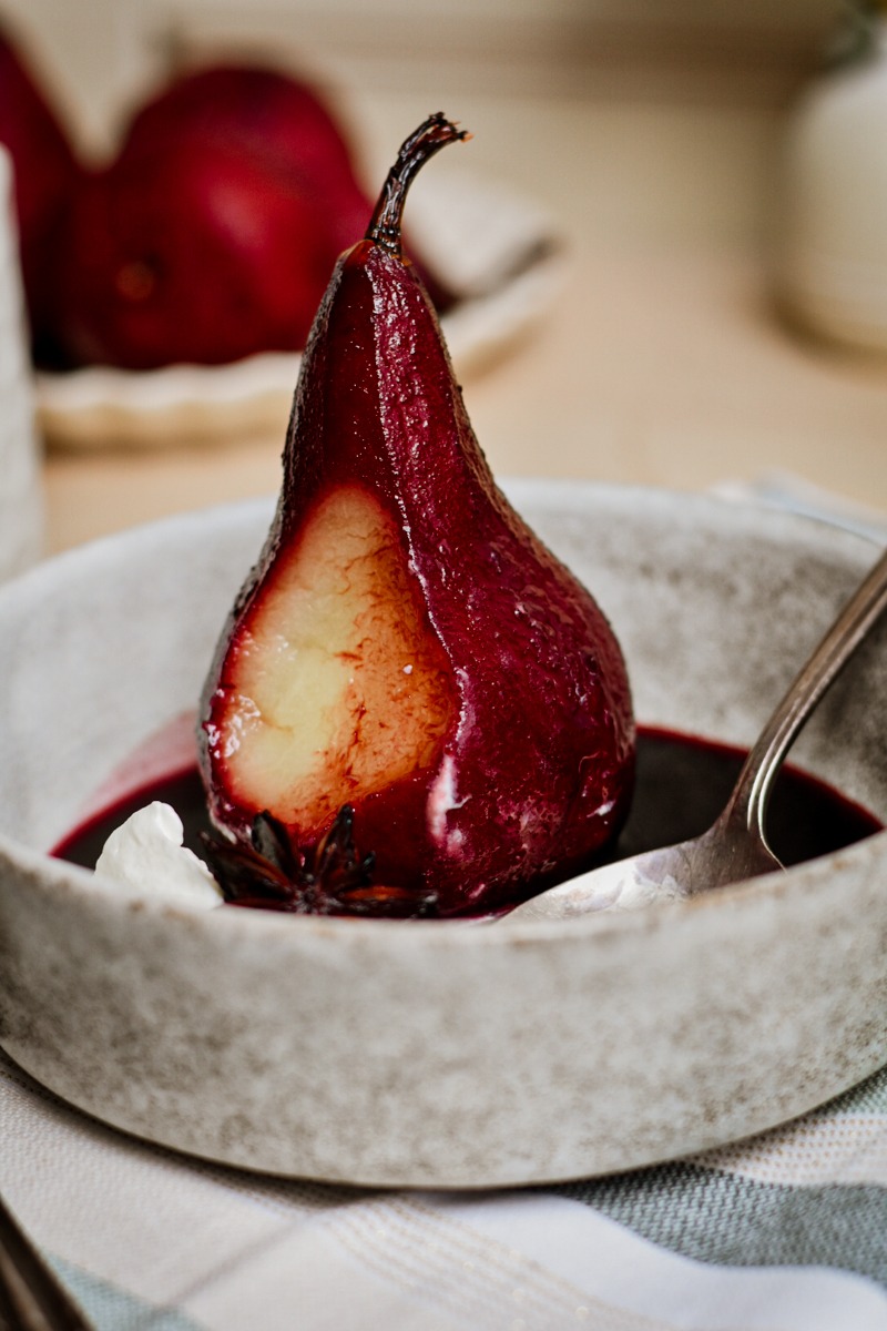 Poached pear in spice red wine served in a bowl with a bite taken from it.
