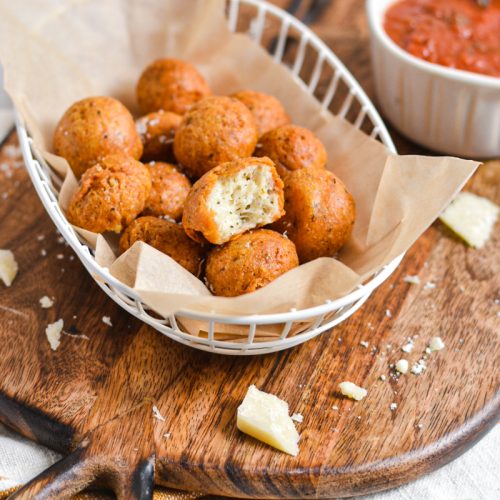 Polpette di parmigiano in a parchment lined basket on a wooden board.