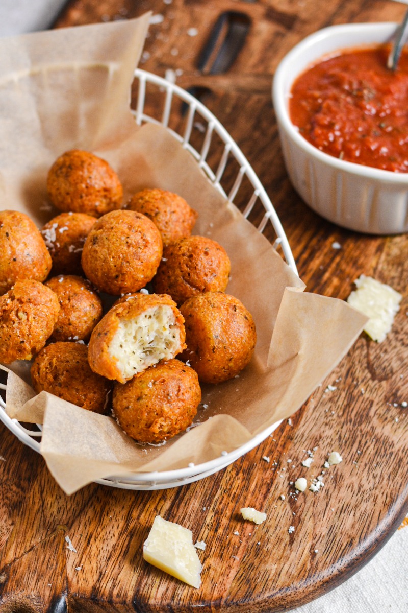 Polpette di parmigiano serbed in a basket with one missing a bite to show the inside.