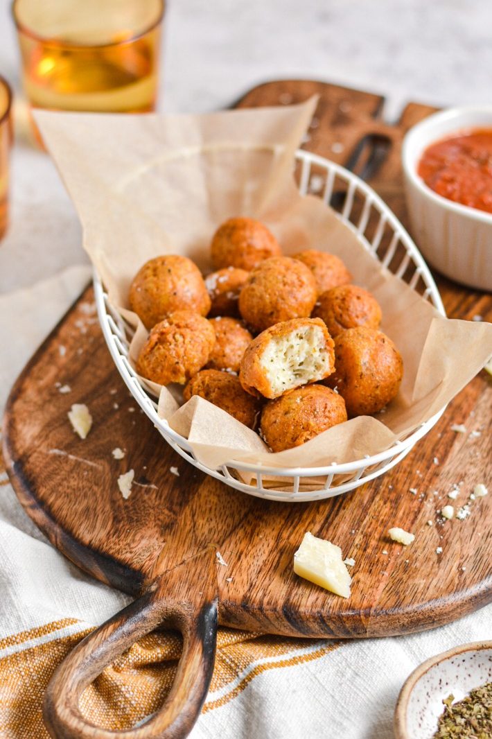 Polpette di parmigiano served in a basket with a side of marinara sauce.