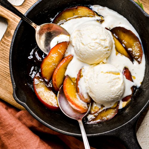 Apples flambe in a skillet with two scoops of ice cream.
