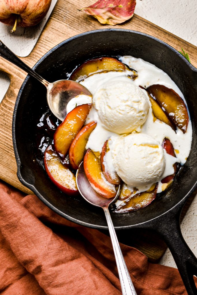 Apples flambe in a skillet with two scoops of ice cream.