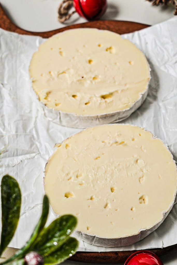 Large wheel of brie cheese slices in half.