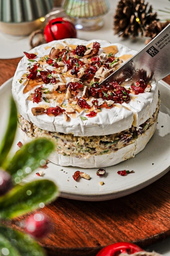 Knife slicing into the cranberry pecan stuffed brie on a plate.