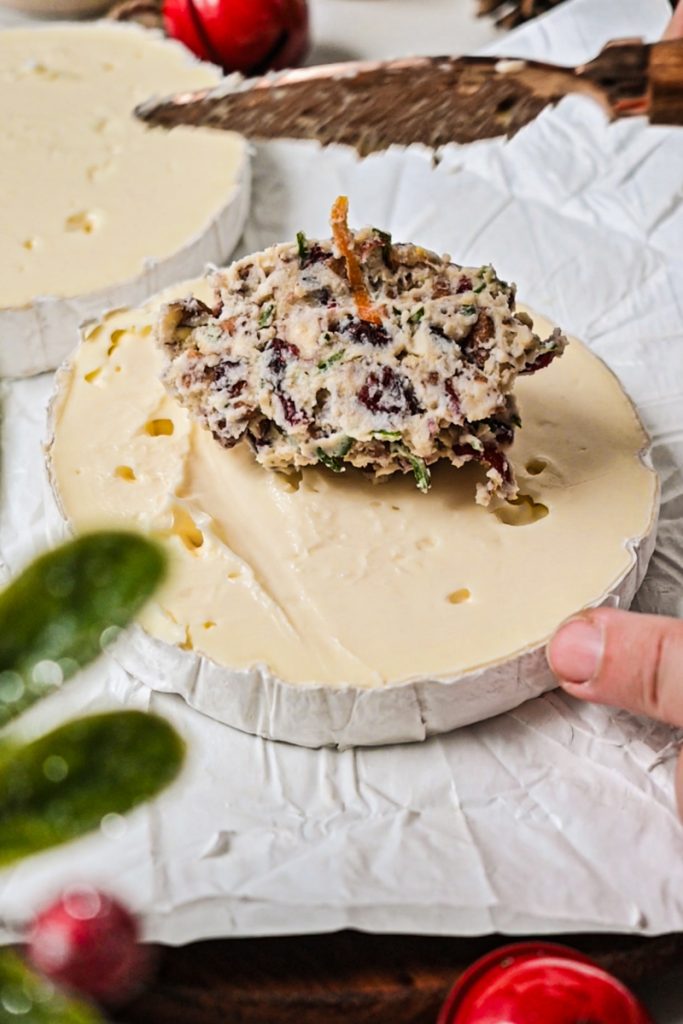 Spreading the cranberry pecan mixture on top of a layer of brie.