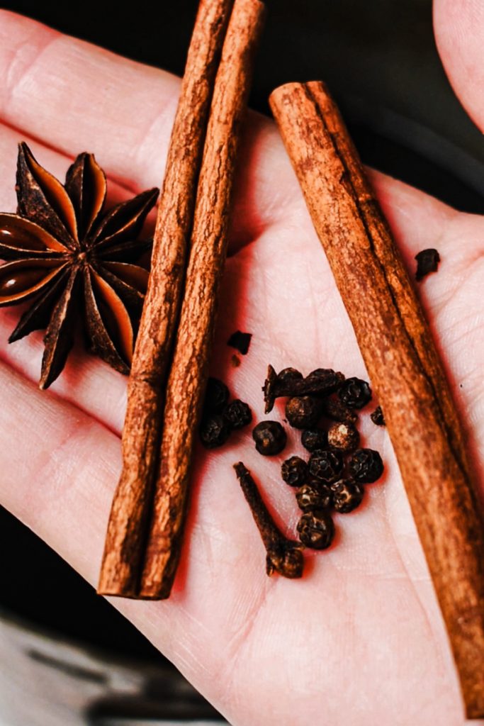 Whole spices like cinnamon, peppercorns, cloves and star anise in a hand.
