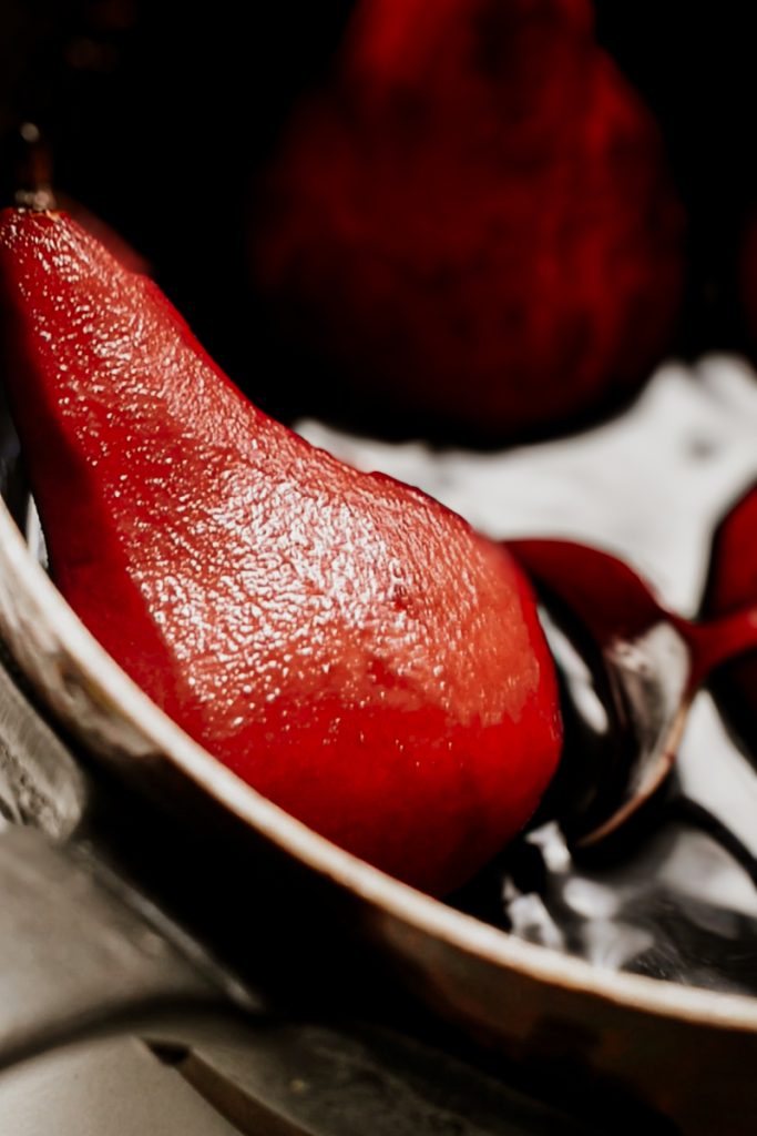 Red wine poached pear in a pot with a spoon scooping it up.