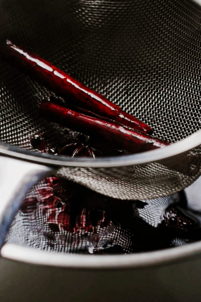 Straining the red wine through a sieve to remove the spices.