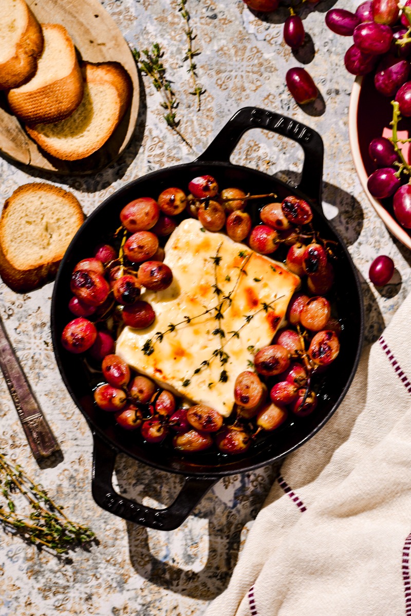 Overhead shot of baked feta with honey and grapes in a cast iron skillet.