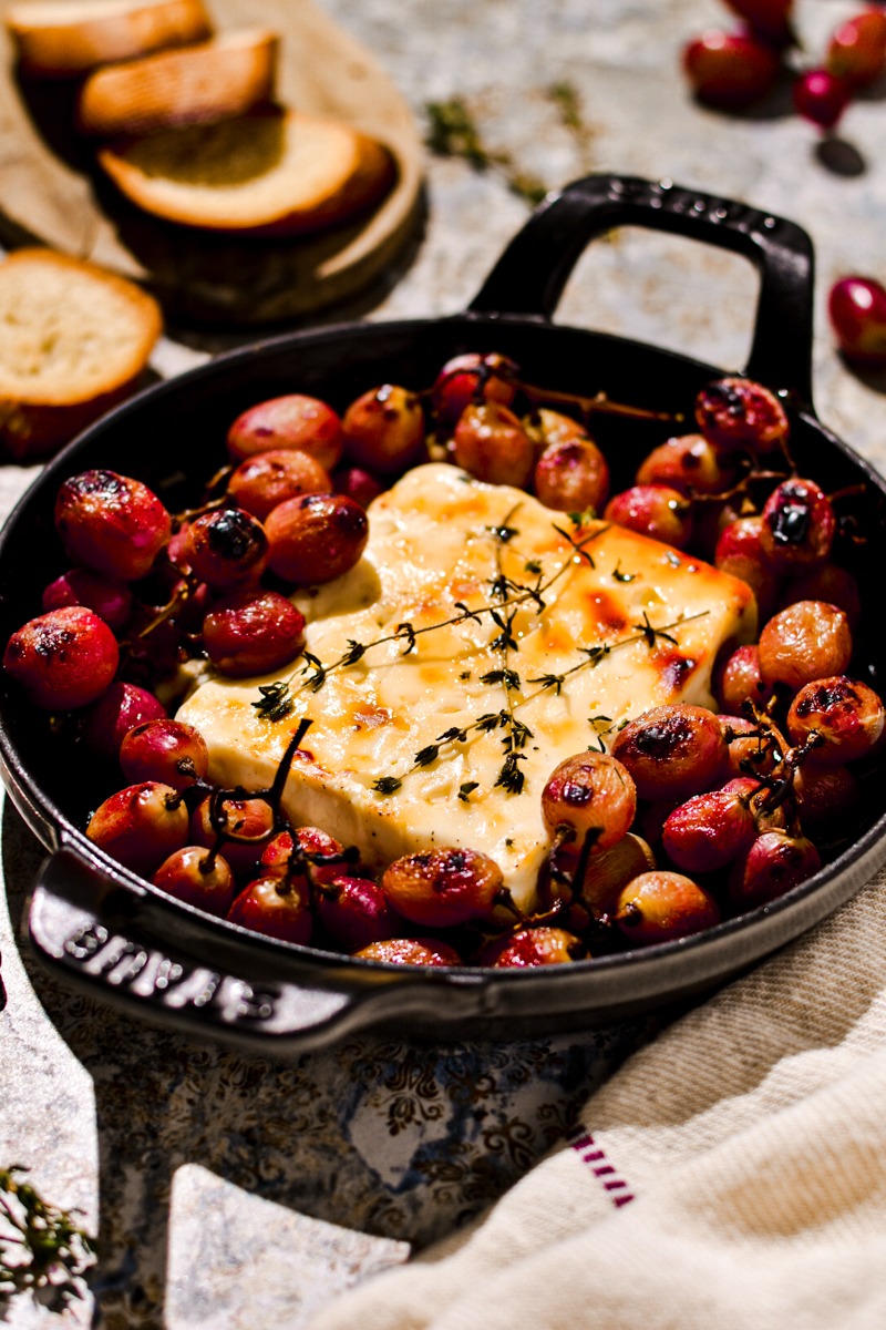 Grapes and a block of feta baked together in a cast iron skillet.