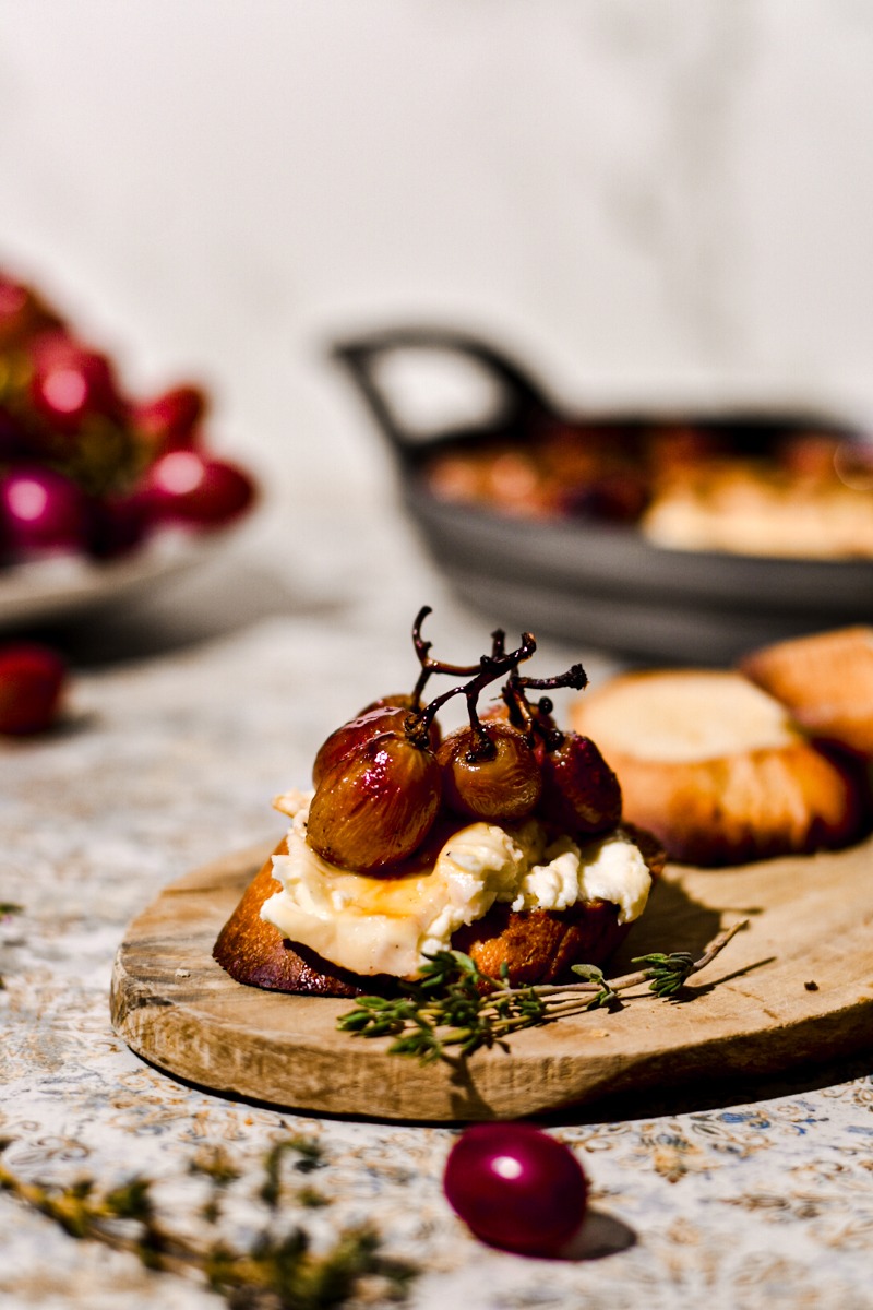 Side view of baked feta smeared onto a crostini with grapes placed on top.