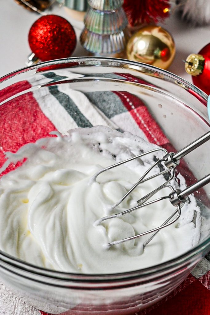 Egg whites whipped in a glass mixing bowl with a hand mixer.