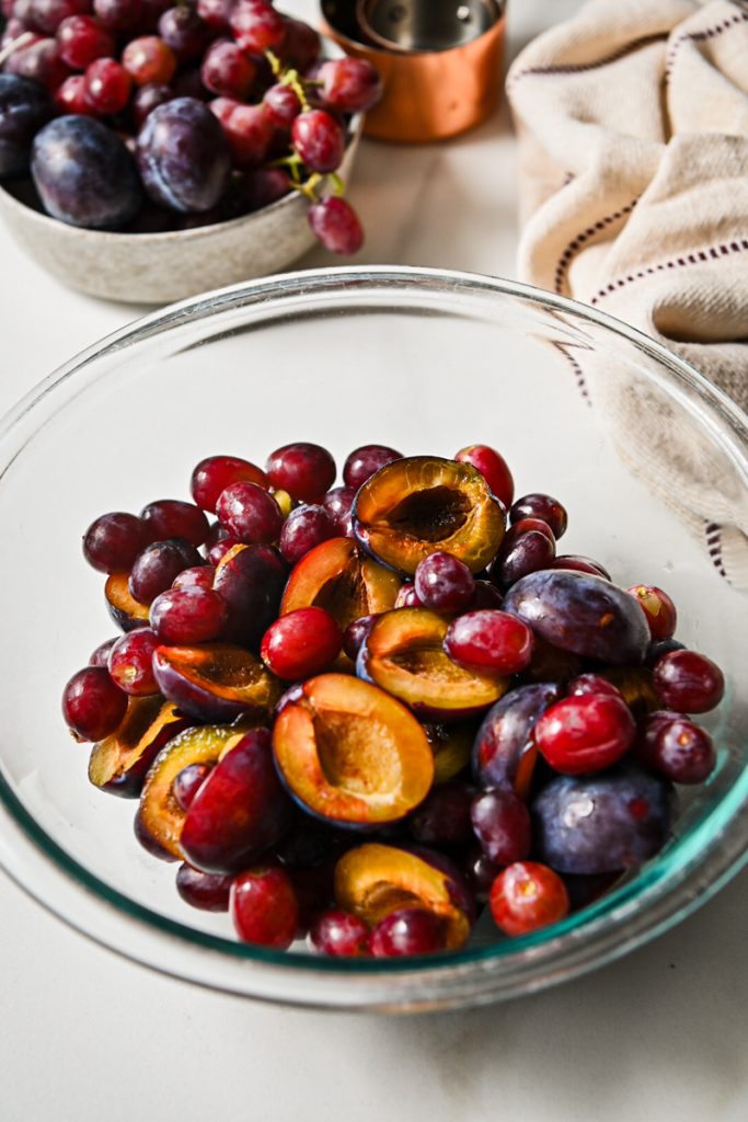 Fresh plums and grapes placed in a glass mixing bowl.