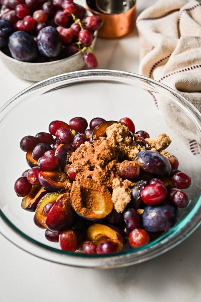 Allspice and brown sugar added to the fruits in a mixing bowl.