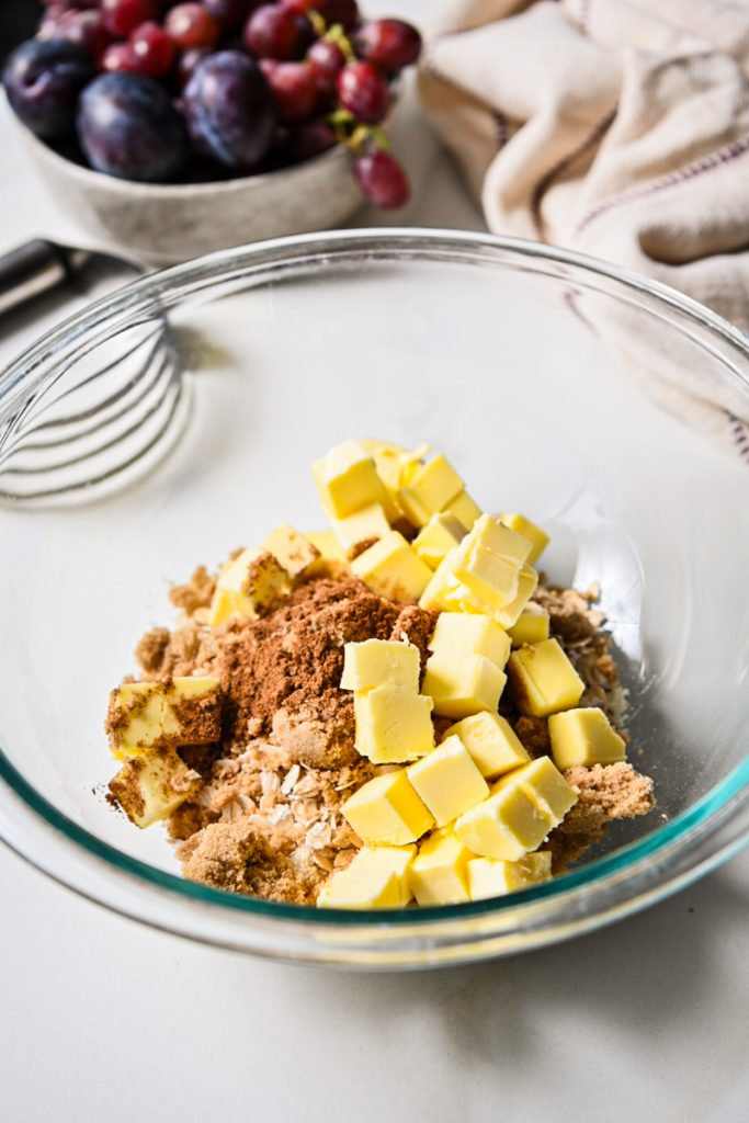 Oat mixture with spices, brown sugar, and cubed cold butter in a mixing bowl.