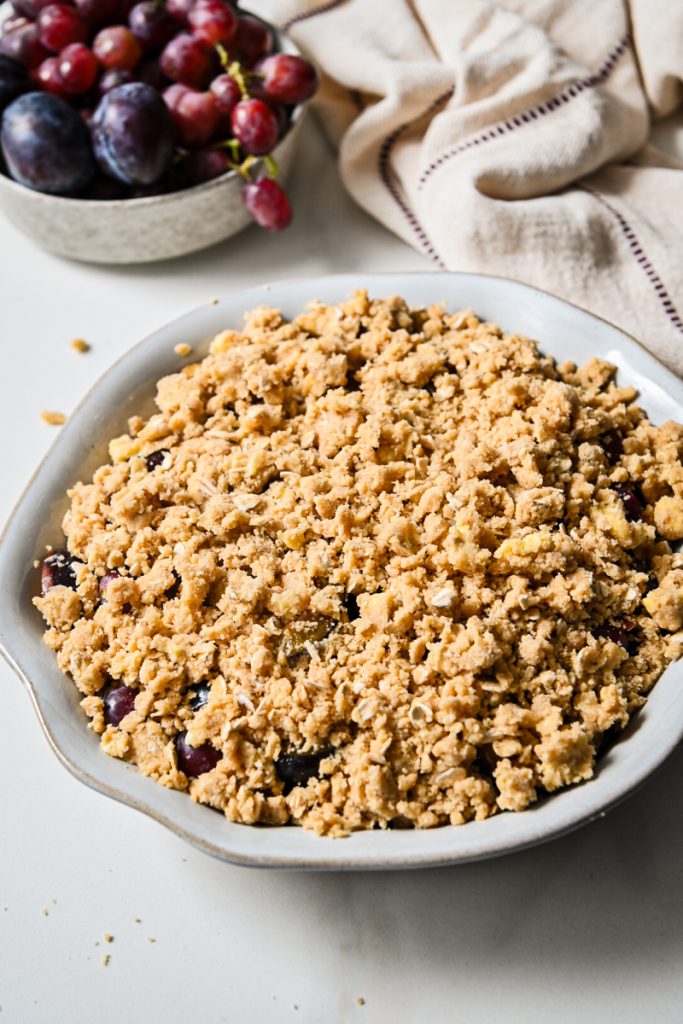Oat crisp mixture on top of the macerated fruits in a pie dish.