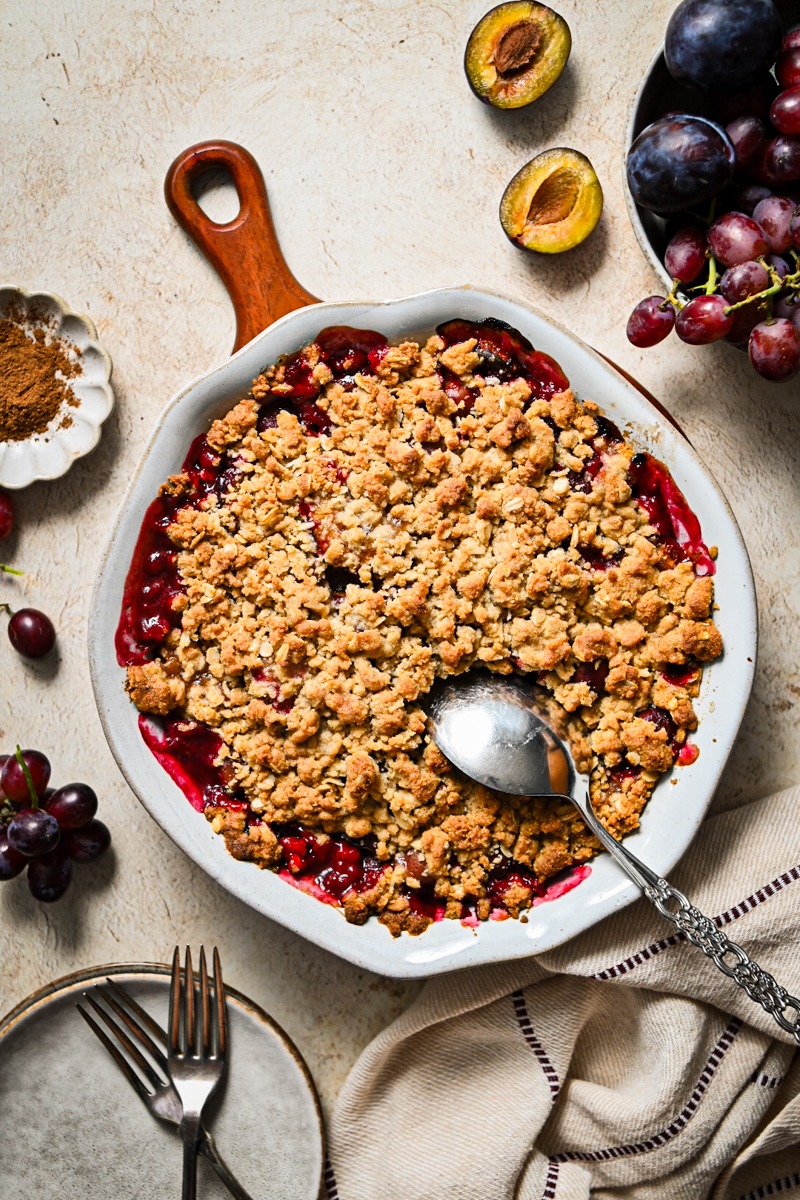 Overhead shot of baked spicy plum and grape crisp with a silver spoon going into the crisp.