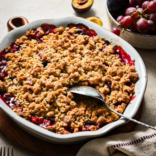Spicy plum and grape crisp in a pie pan after being baked with a silver spoon sticking into it.