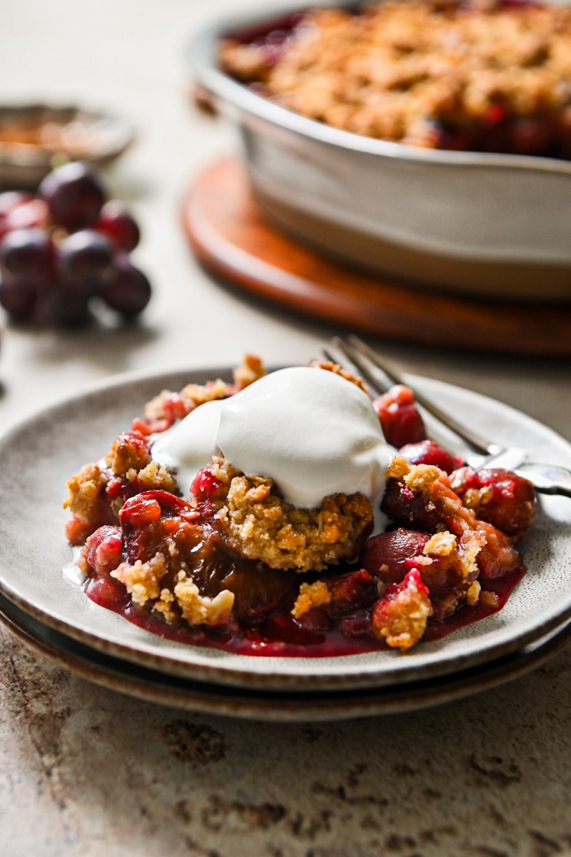 Portion of plum and grape crisp served on a plate with ice cream on top.