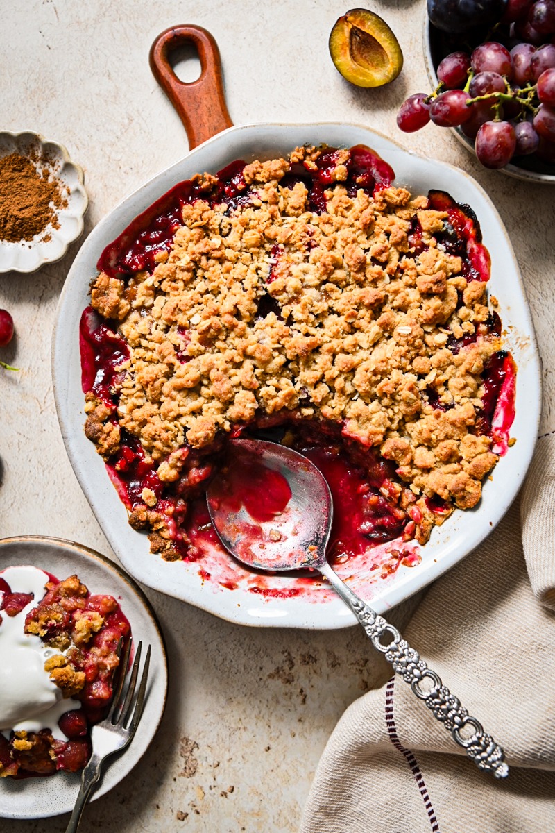 Spicy plum and grape crisp in a pie dish with a portion missing.