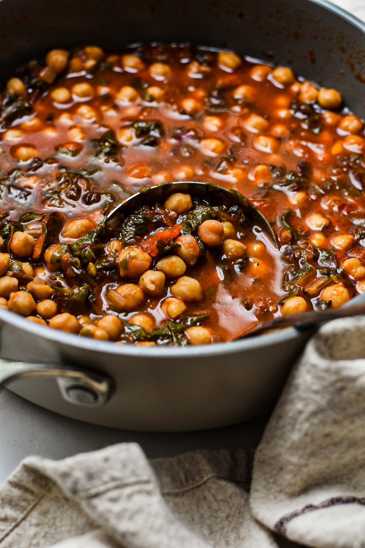 Large pot of chickpea soup with Swiss chard with a large ladle in the pot.