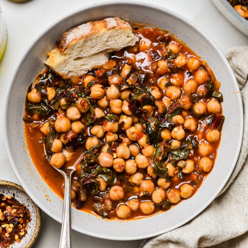 Overhead shot of a bowl of chickpea soup with Swiss chard with bread on the side.