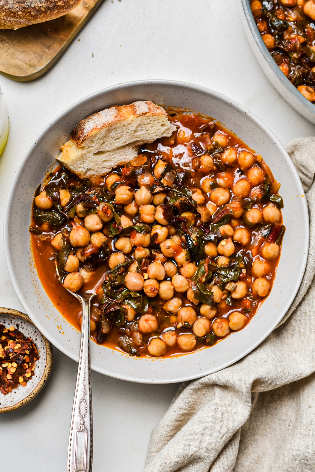 Overhead shot of a bowl of chickpea soup with Swiss chard with bread on the side.