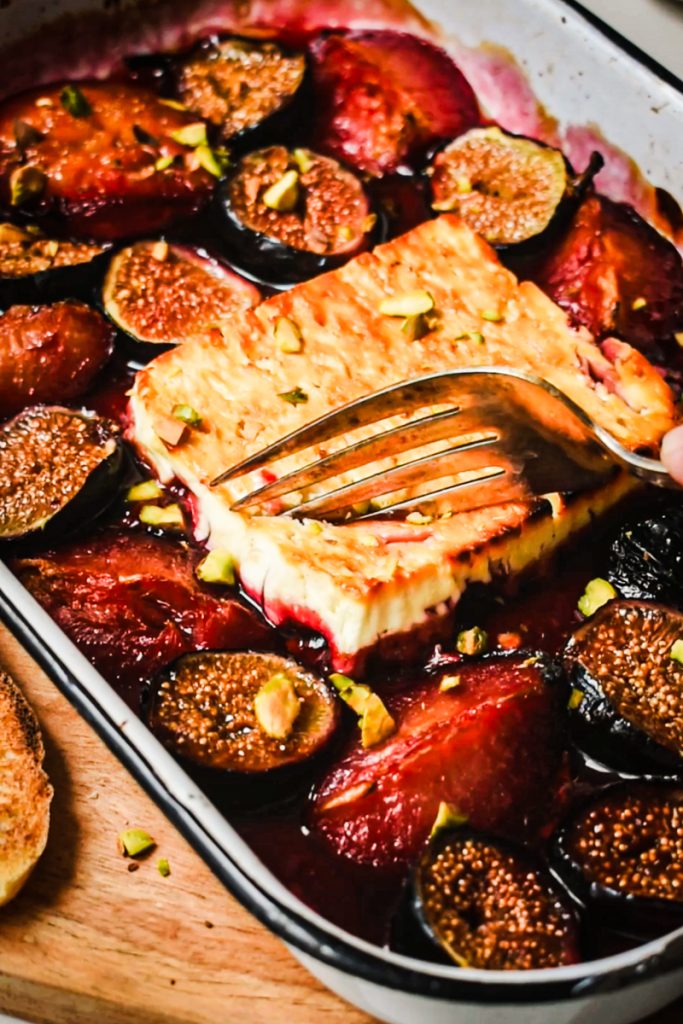 A fork breaking into the baked feta in a baking dish.