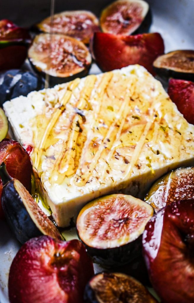 Feta with plums and figs in a baking dish before roasting.