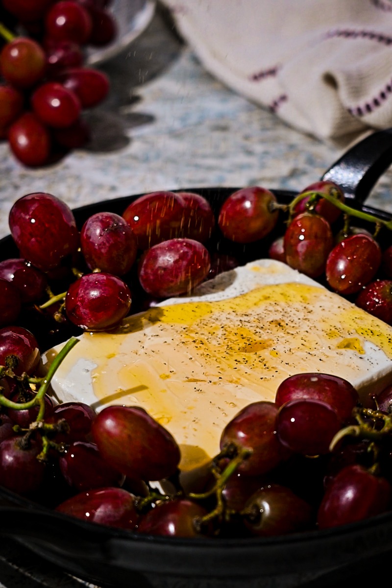 Pepper sprinkled on top of the block of feta surrounded by grapes.