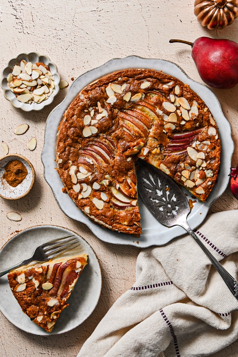 Spiced pear French cake on a serving dish next to a slice of it on a plate.