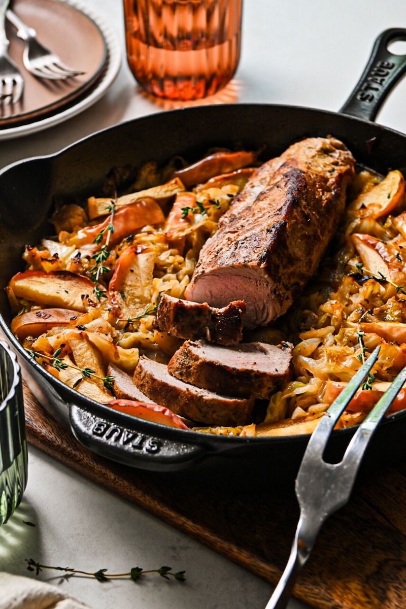 Side view of a cast iron skillet with cabbage and apples and a pork loin in the middle.